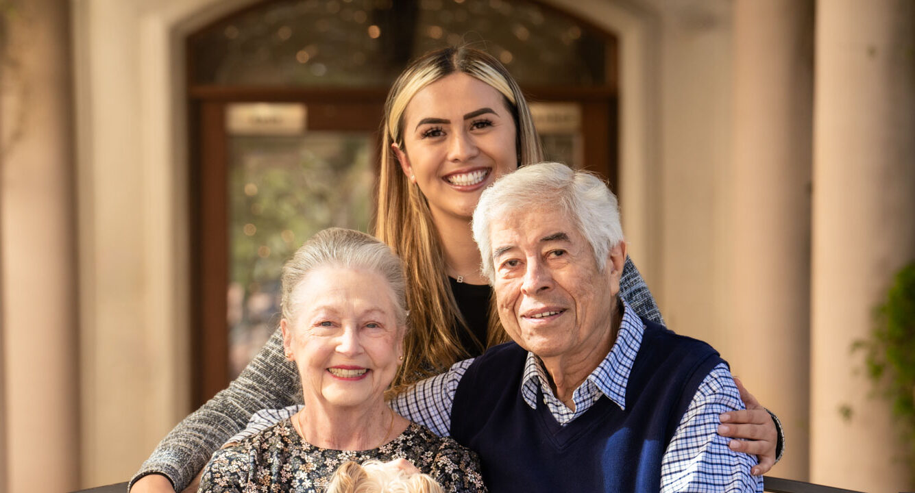 young woman smiling for photo with older couple holding small dog