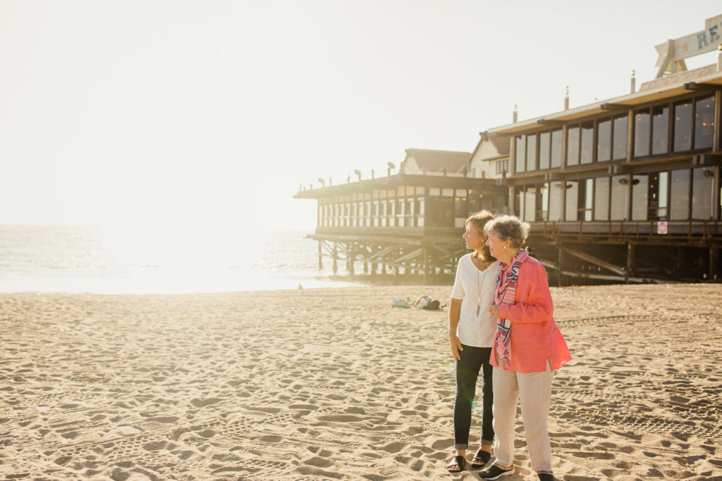 two people on the beach watching the ocean during sunset